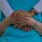 A close-up of hands belonging to two people, showing affection and care, with a soft green background.